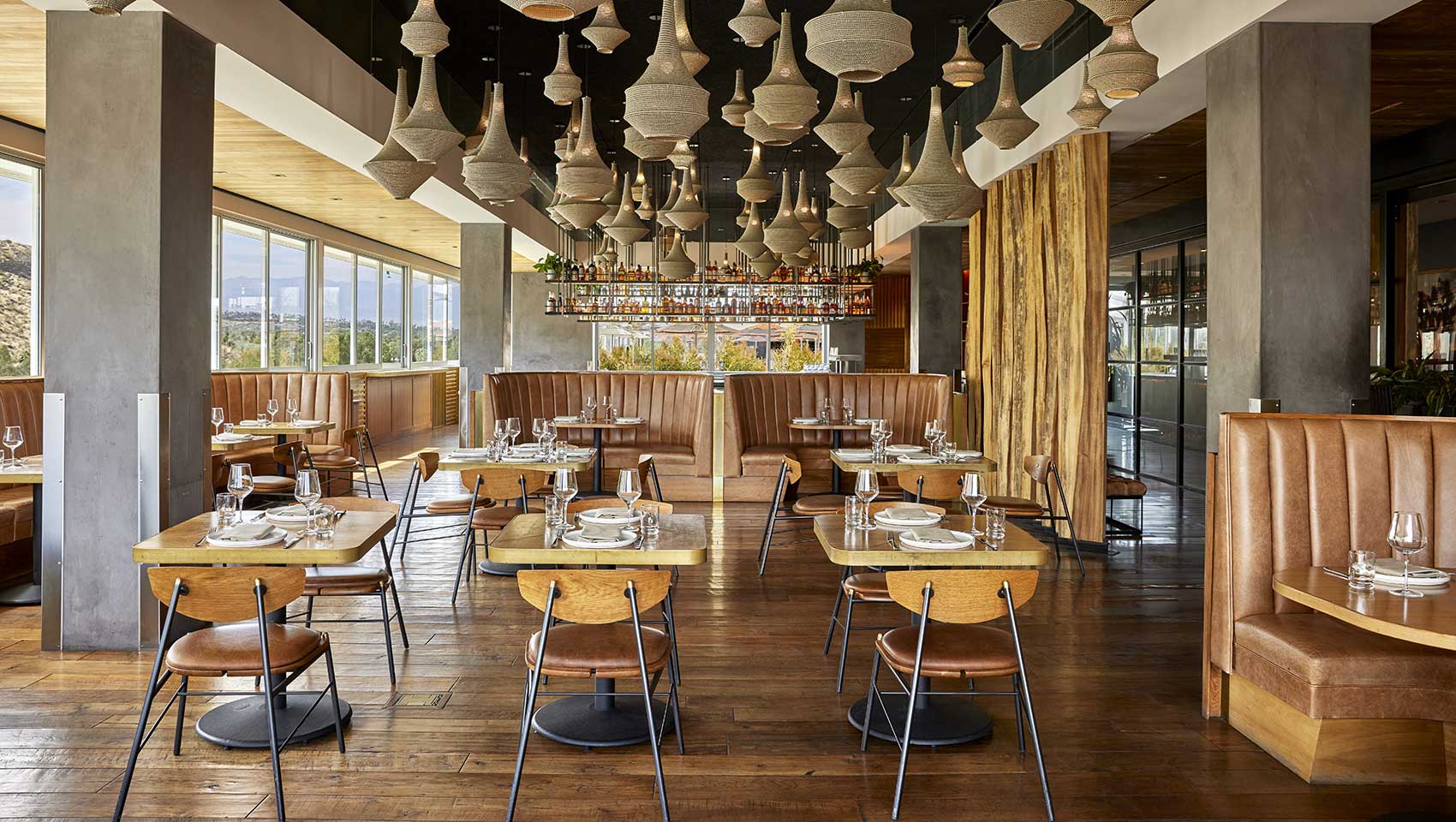 Restaurant interior with brown leather booths, woven chandelliers, and views of the surrounding desert mountainside