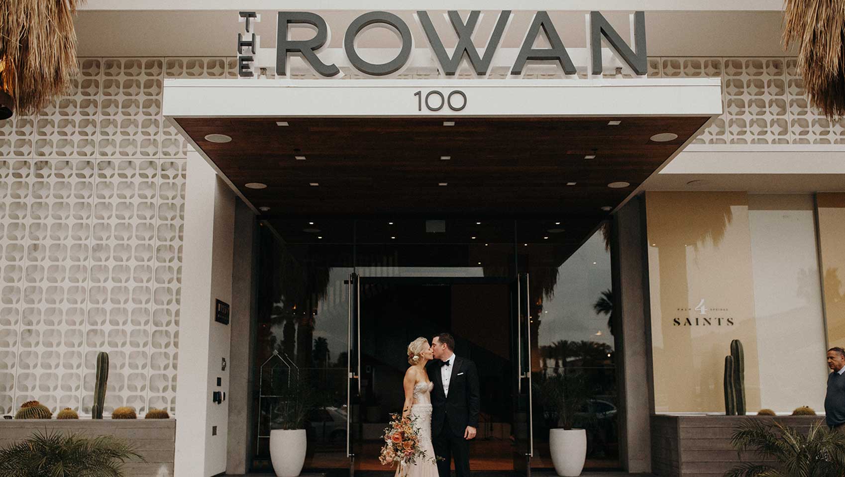 A couple on their wedding day kiss in front of the entrance to the Rowan hotel