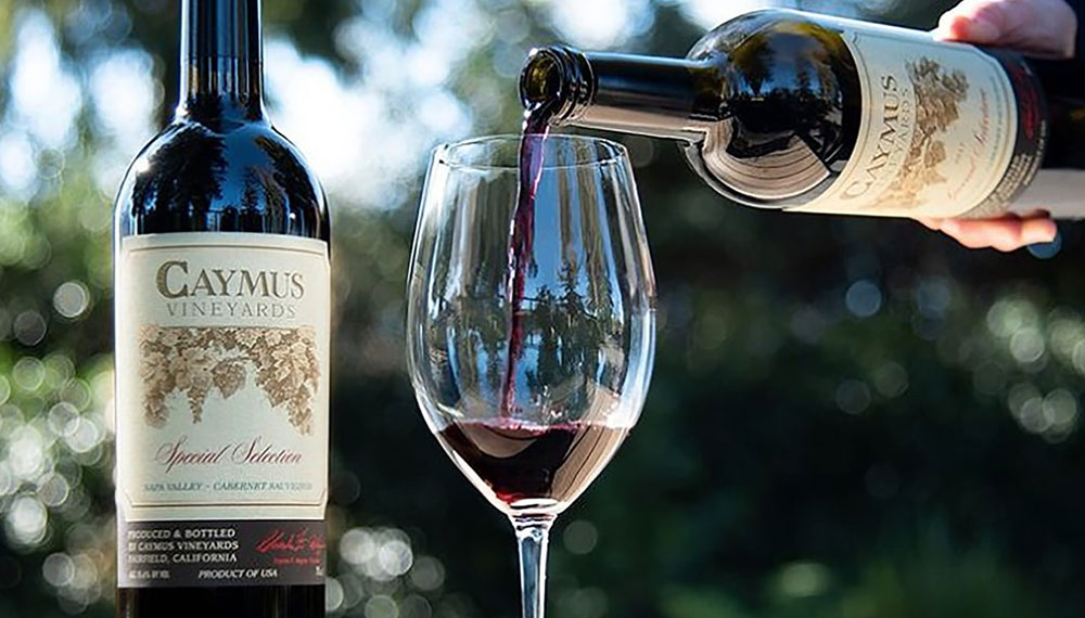 Bottle of Caymus red wine being poured in front of scenic vinyard background