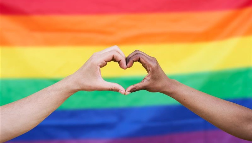 2 hands making a heart in front of a pride flag